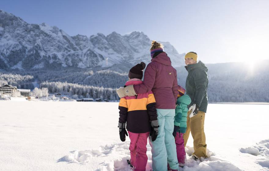 Familie steht im Schnee mit Blick auf die Zugspitze