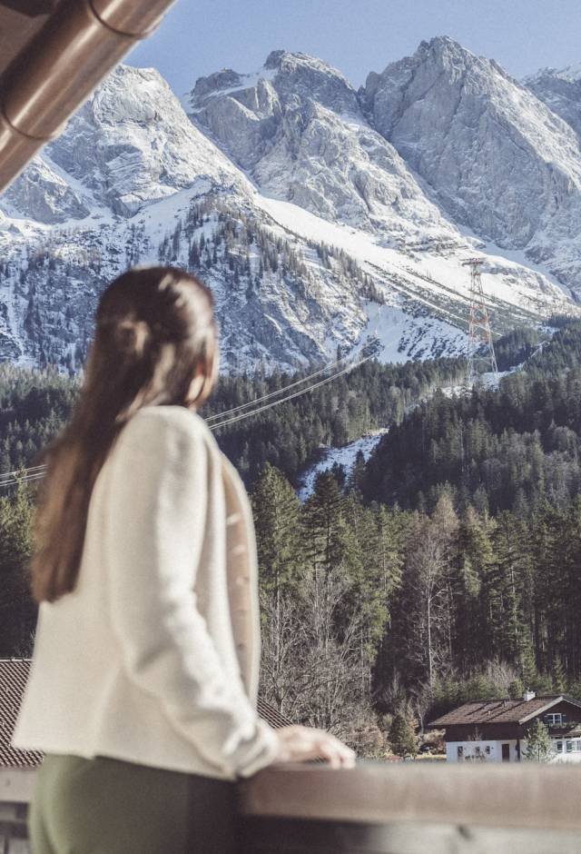Frau steht auf Balkon mit Blick auf die Zugspitze
