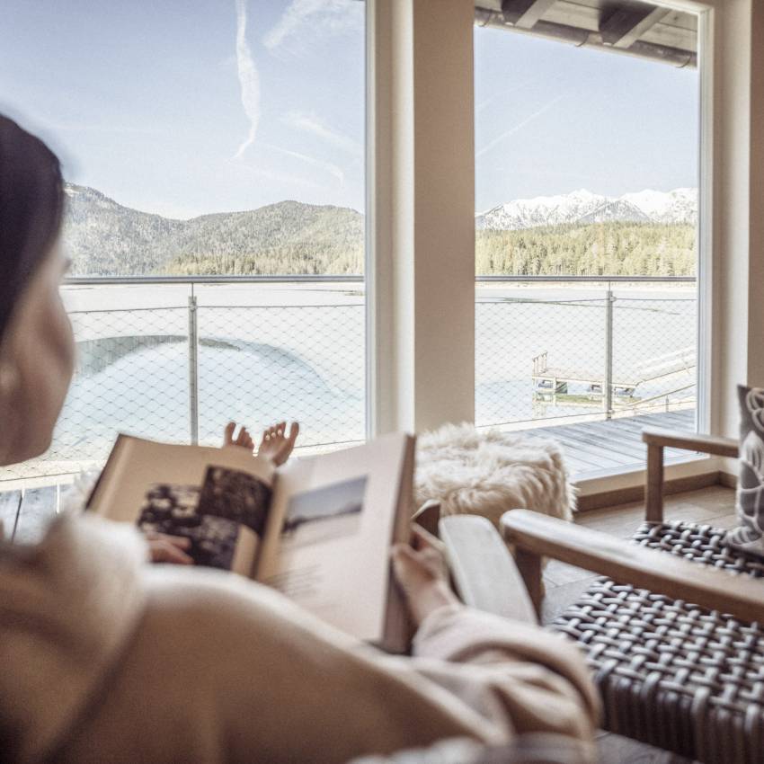 Frau liest im Ruheraum ein Buch mit Blick auf den Eibsee