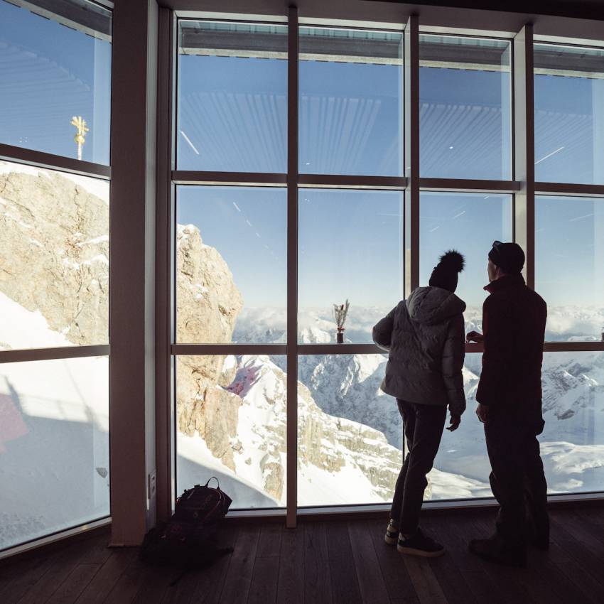 Mann und Frau stehen am großen Fenster blicken auf die Zugspitze